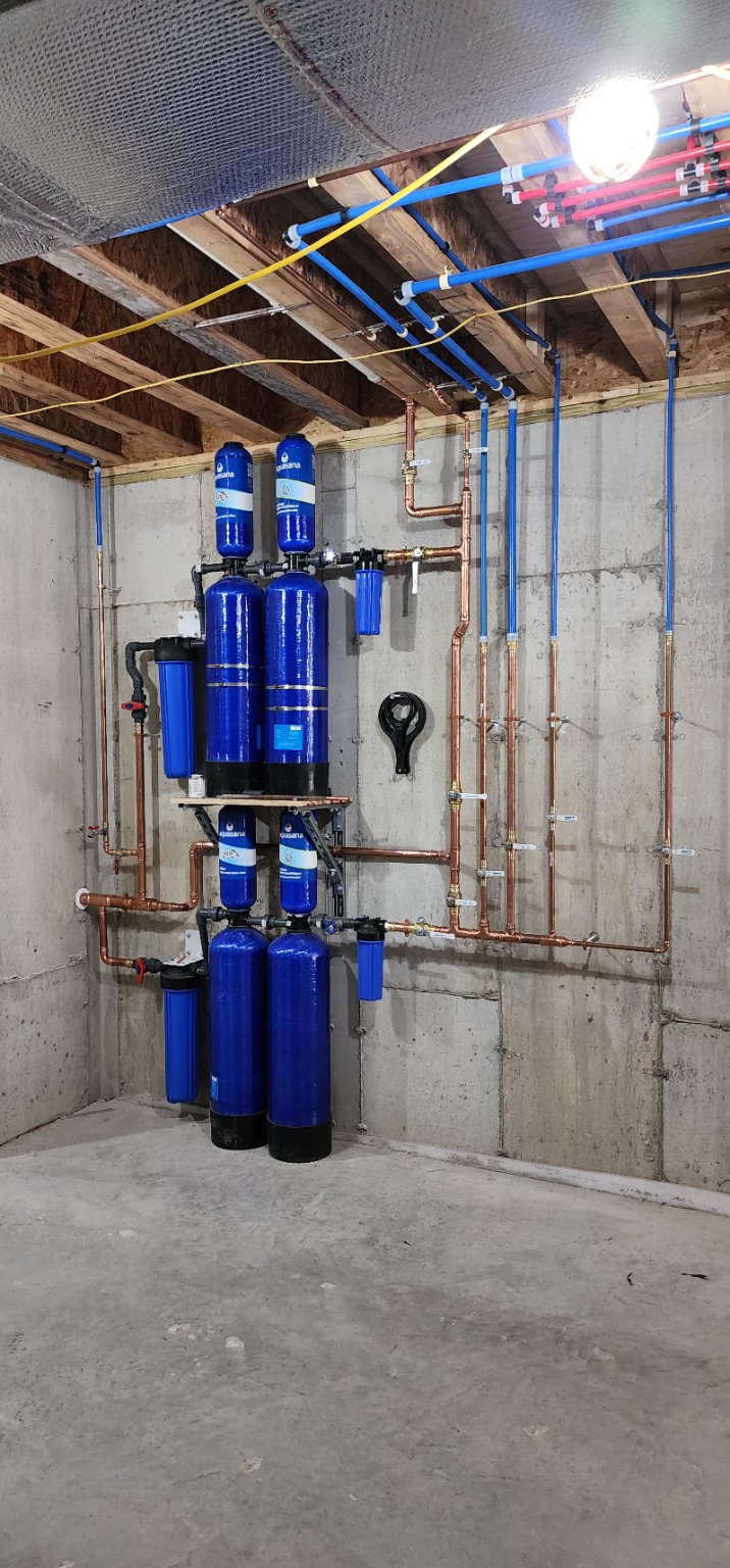 Whole-house water filtration system with blue filter tanks, copper piping and PEX lines